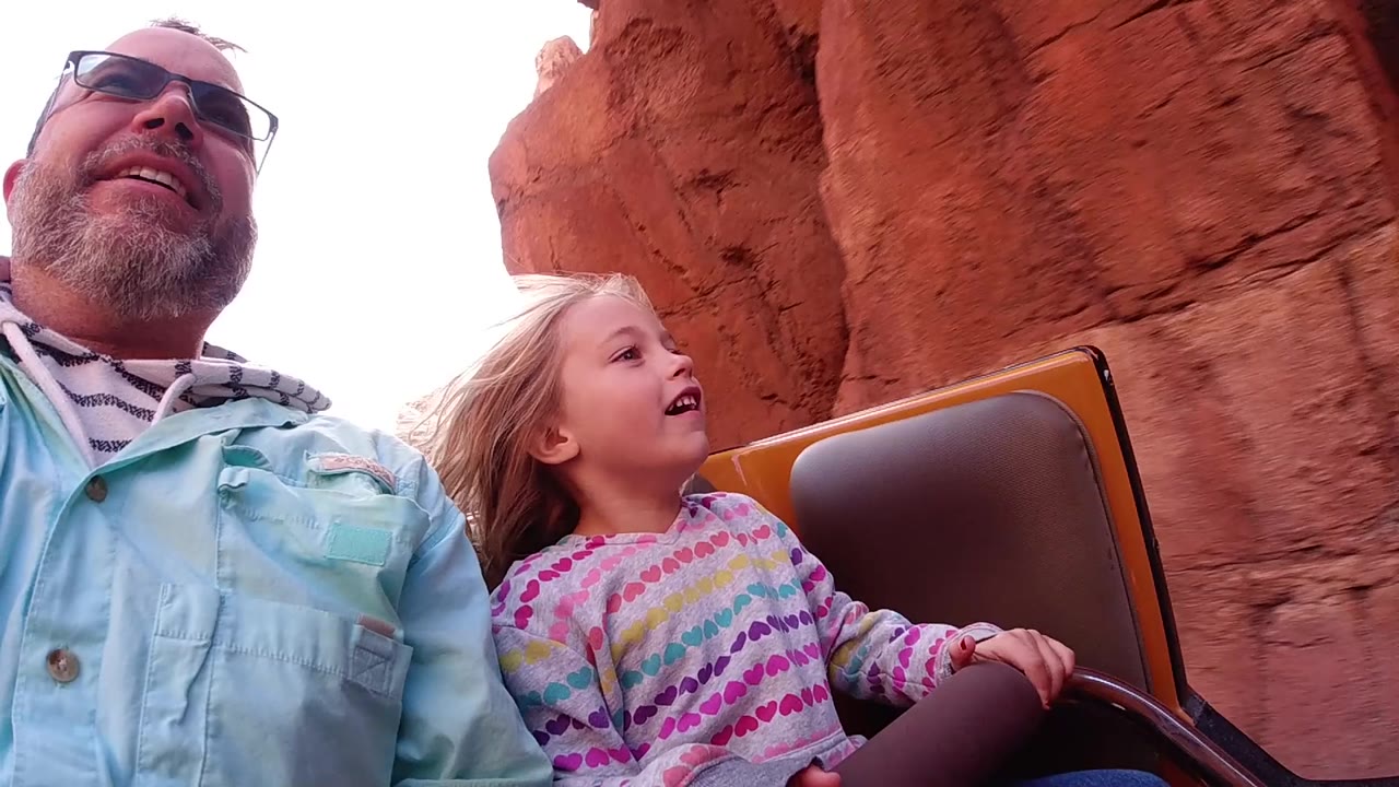 Child smiles while seated next to a man on the coaster.