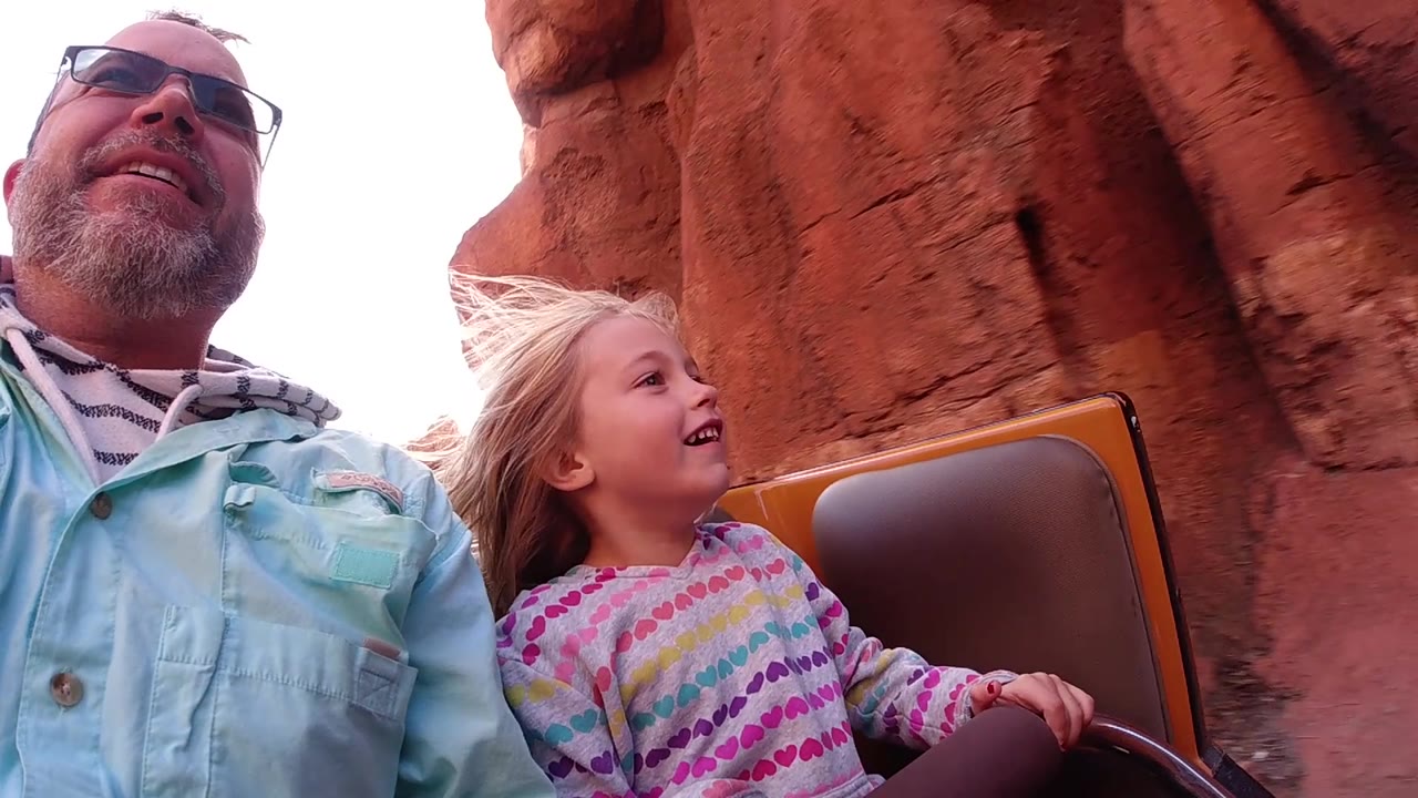 At Disneyland California, the riders remain close to camera as the red rock wall fills more of the background behind the child's windblown hair.