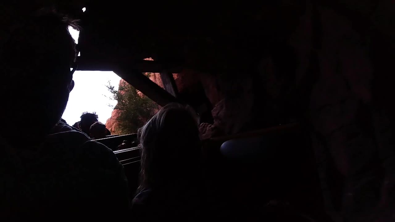 Inside a dark Disneyland California ride vehicle, silhouetted riders sit ahead while daylight pours through an opening near reddish rock-like walls.