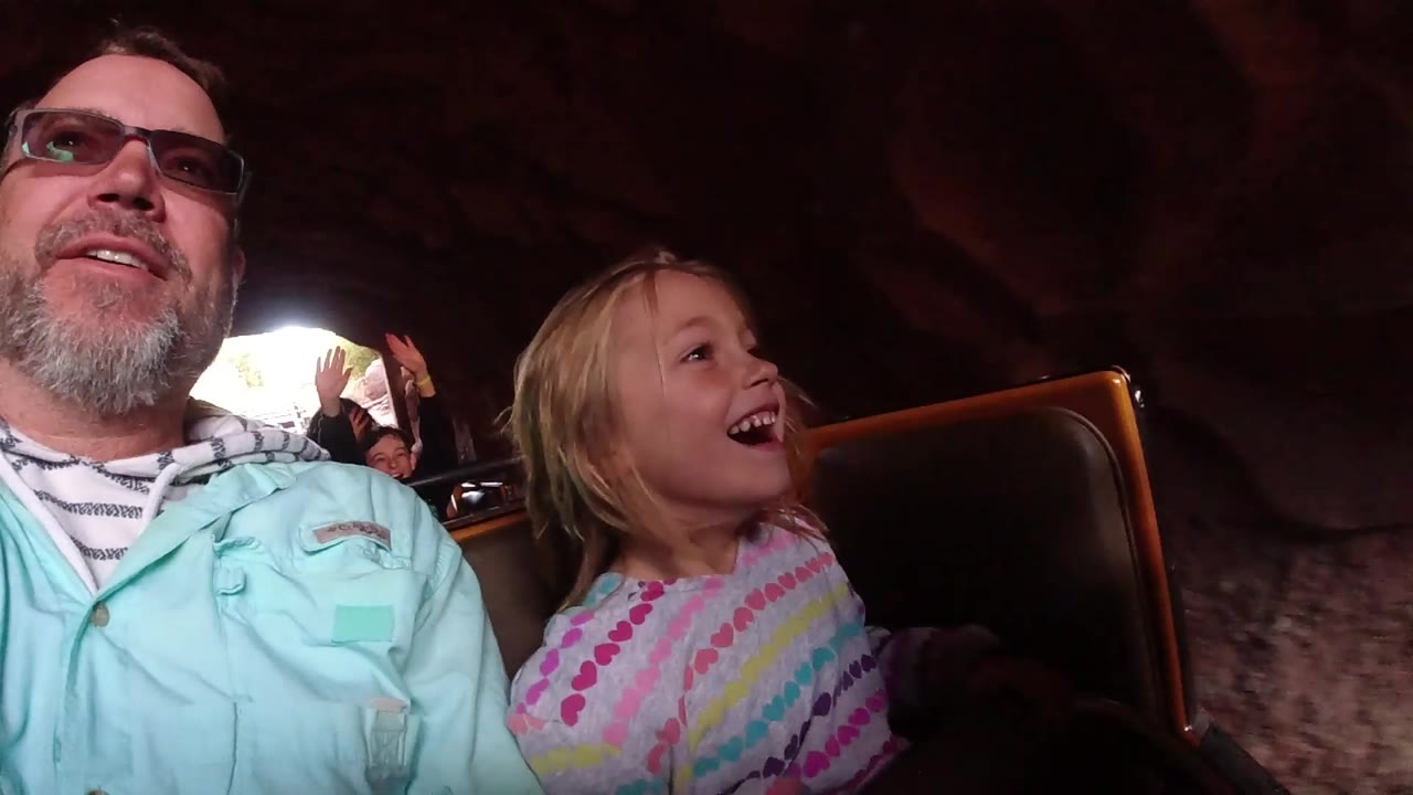 Smiling girl beside her father inside a rock-walled ride area.
