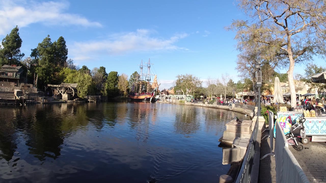 Wide waterfront view with tree reflections, railing, stroller, and ship across the lake.