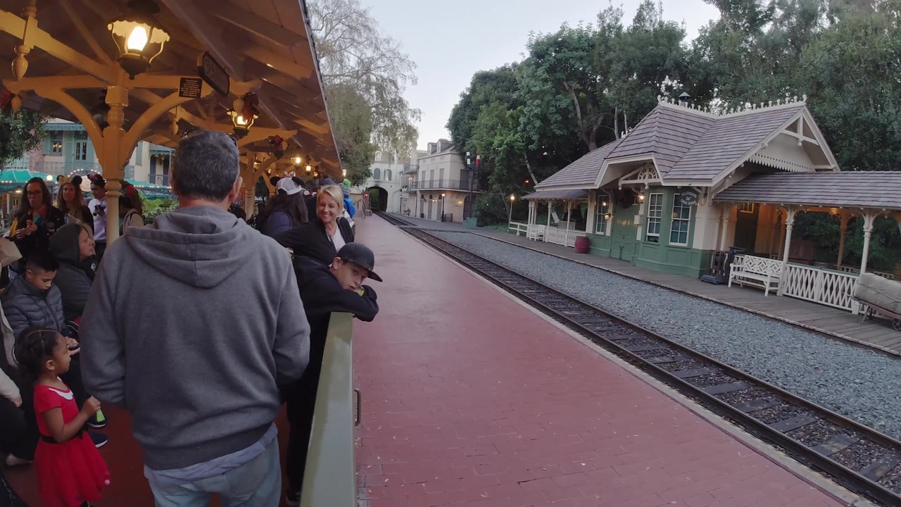Guests remain gathered under the roof at Disneyland California, with a child near the railing and the empty tracks stretching toward the station area.