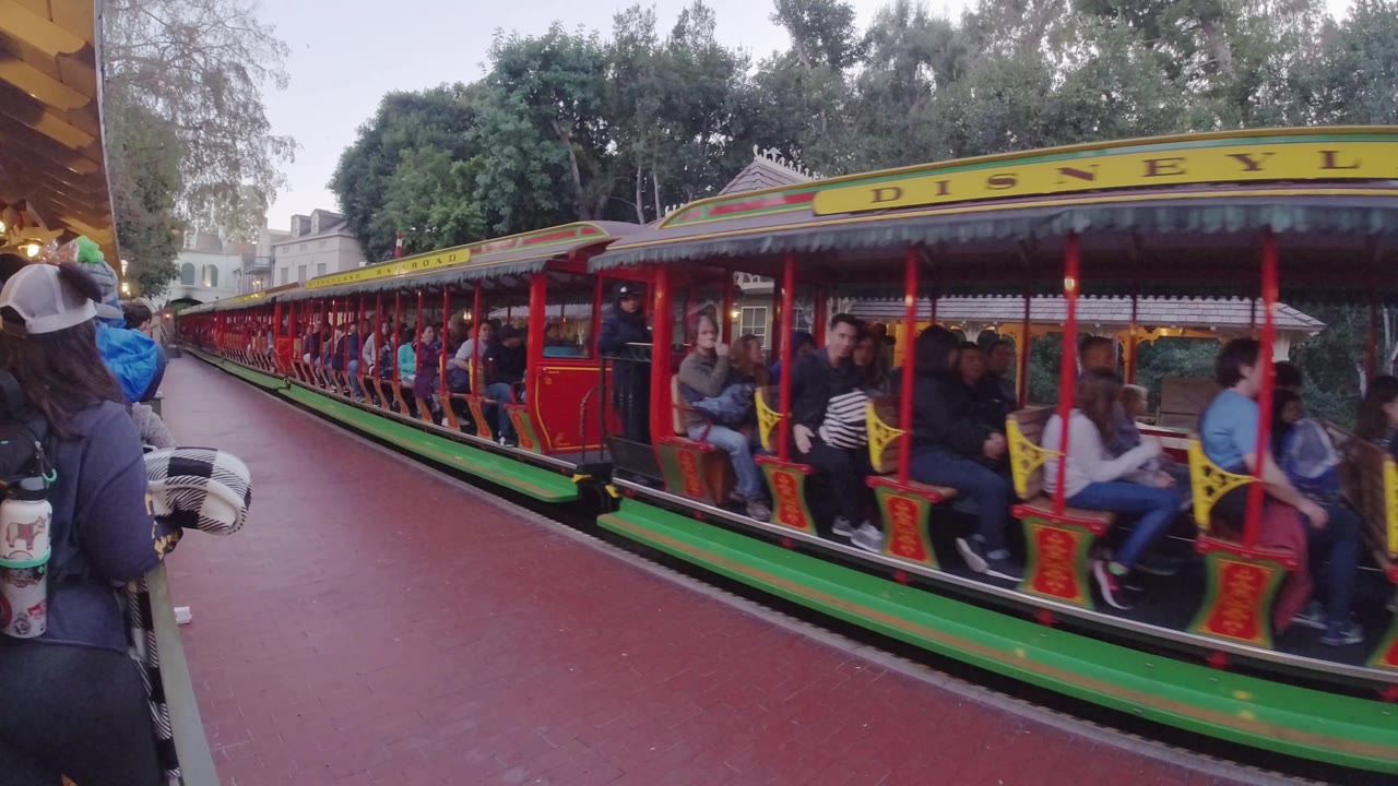 Open-sided train cars full of riders next to a red platform.