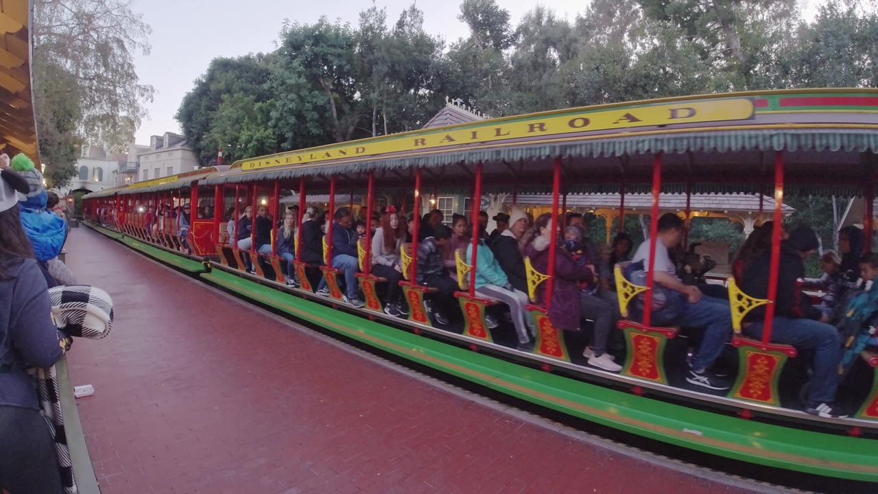 Long red and green Disneyland train with guests in open cars.