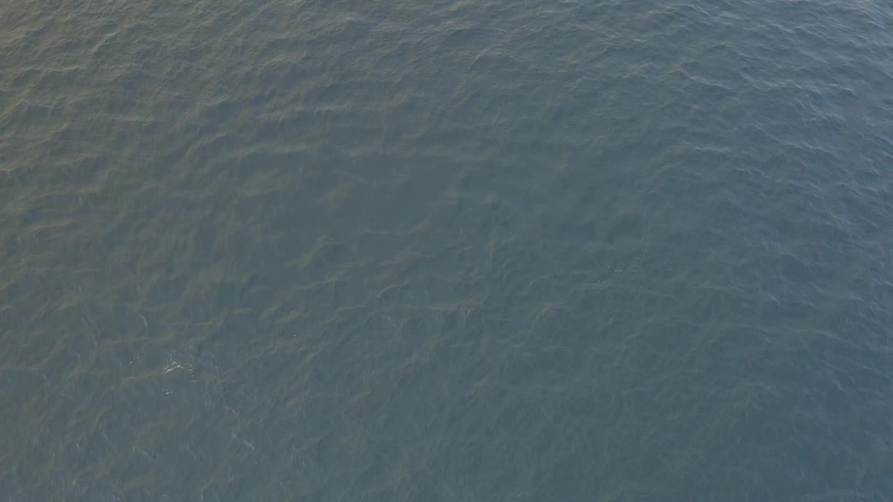 At one second, rippled ocean water in Baja California Sur shows more pronounced dark green shapes under the surface, with no shoreline or visible people.