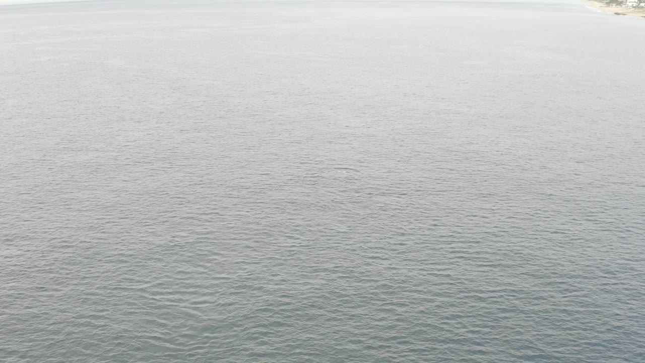 Grey daylight falls across the rippled lake in Baja California Sur, with a narrow pale land strip just visible near the top and no visible people.