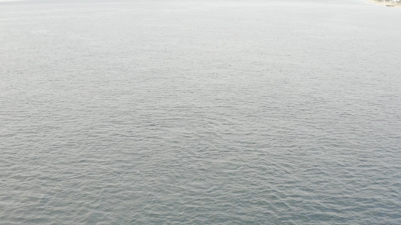 Aerial frame from Baja California Sur with pale blue green ocean filling the view, faint shoreline along the top edge, and no visible people.