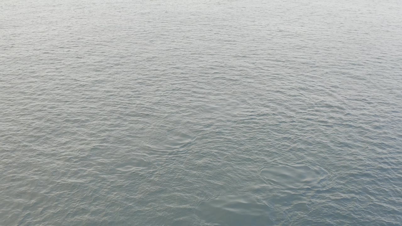 Close view of muted gray-green water in Baja California Sur with darker ripple patches and a broad empty surface, with no visible people.
