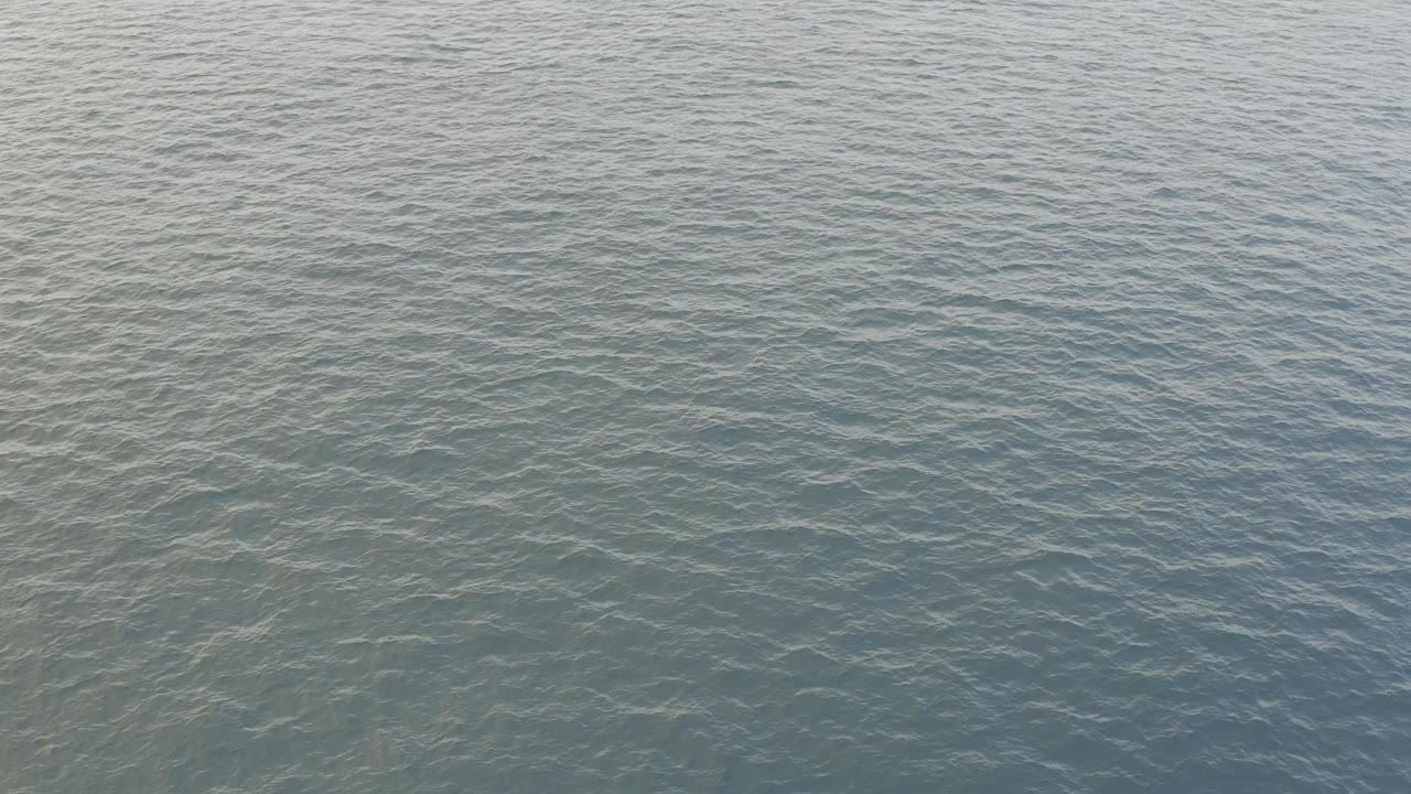 High-angle aerial frame over Baja California Sur ocean water, showing blue ripples and muted green areas with no visible people.