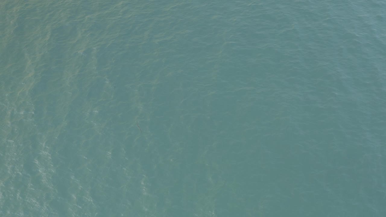 A blue-green ocean surface in Baja California Sur shows darker vertical underwater bands beneath the rippled water, with no visible people.