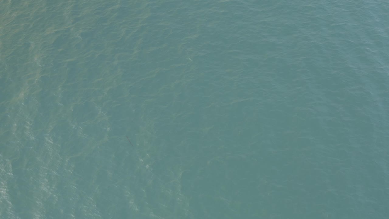 Muted teal seawater fills the Baja California Sur frame with low wavelets, hazy submerged shapes, and no visible people.
