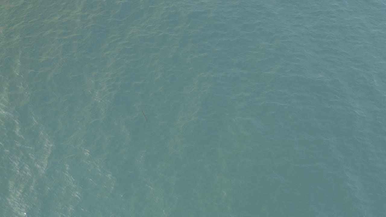 Teal coastal water in Baja California Sur, Mexico, shows soft diagonal shimmer patterns and faint darker shapes below the surface, with no visible people.
