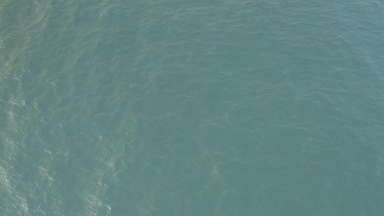 Aerial frame over turquoise water in Baja California Sur, showing soft ripple lines and cloudy shallow patterns with no visible people.
