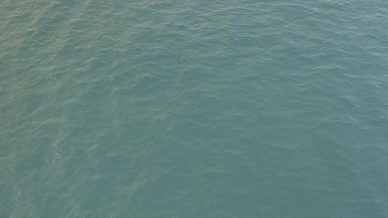 Direct-down aerial frame of Baja California Sur water with small wavelets and muted sandy-toned streaks below the surface, with no visible people.