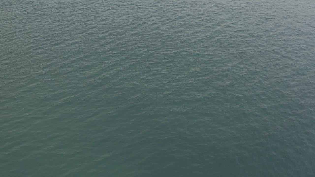 Aerial ocean view in Baja California Sur, Mexico, with faint diagonal wave patterns over teal water and no visible people.