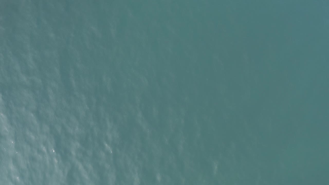Downward aerial view of teal ocean water in Baja California Sur, Mexico, with faint surface ripples and no visible people.