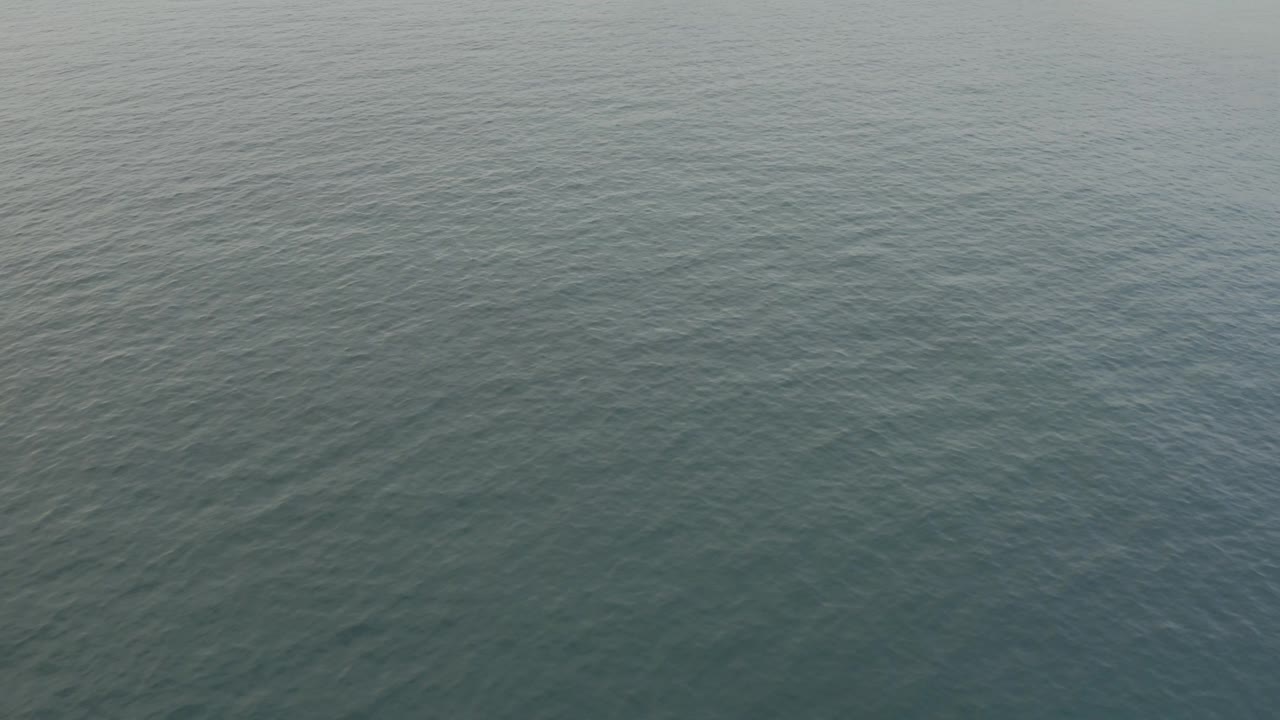 Aerial view over blue-green water toward the sandy Baja California Sur shoreline near the top of frame, with no visible people.