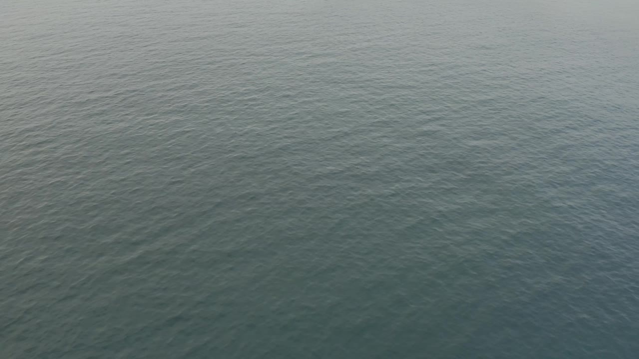Aerial frame of rippled sea off Baja California Sur with a pale beach corner entering at the upper right, and no visible people.