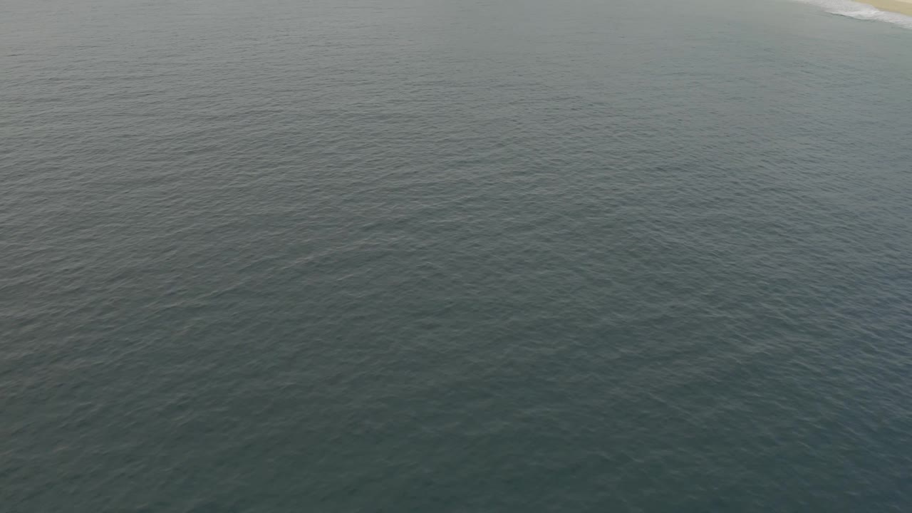 Wide aerial frame in Baja California Sur showing textured ocean water with a thin beach line near the top and no visible people.