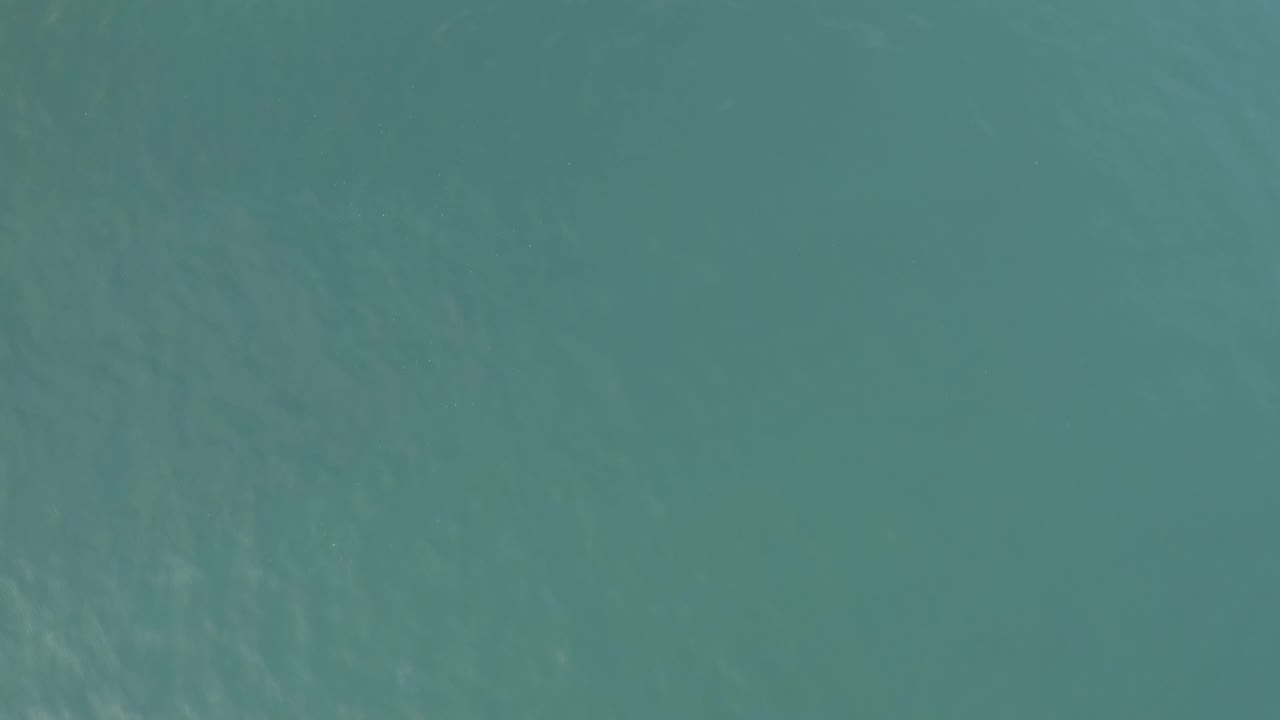 Aerial straight-down frame of Baja California Sur ocean water, showing muted blue-green color and soft diagonal ripple marks with no visible people.