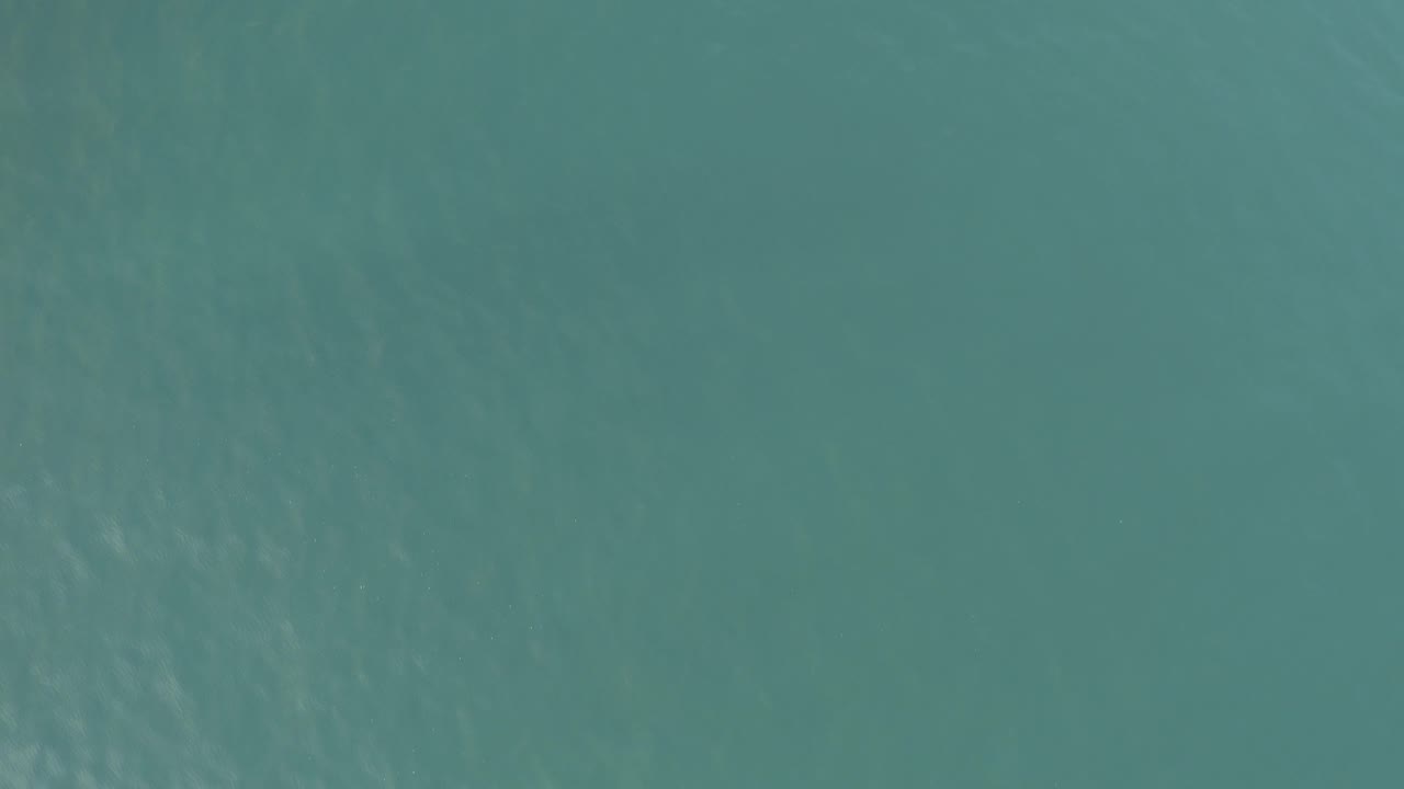 Calm blue-green ocean surface in Baja California Sur, Mexico, viewed from above with pale wavering patterns and no visible people or objects.