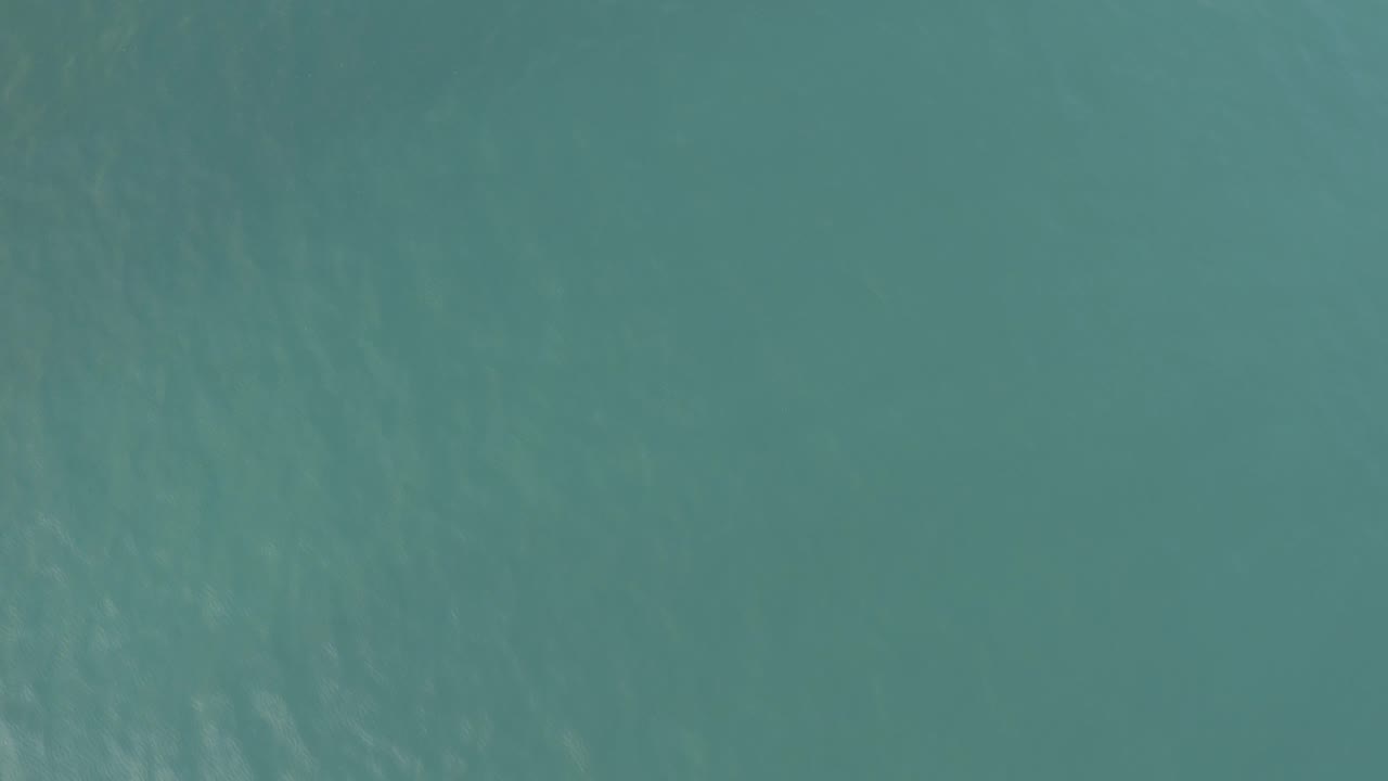 Straight-down ocean view from the Baja California Sur clip, with darker teal patches and gentle surface ripples, no boats, land, or visible people.