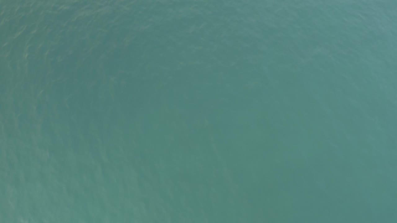 High-angle aerial view of turquoise-green water in Baja California Sur, Mexico, with faint surface texture and no visible people.