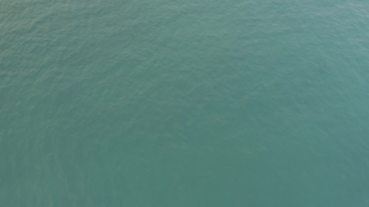 Drone-like overhead view of pale green-blue ocean in Baja California Sur, Mexico, showing fine surface texture and no visible people.