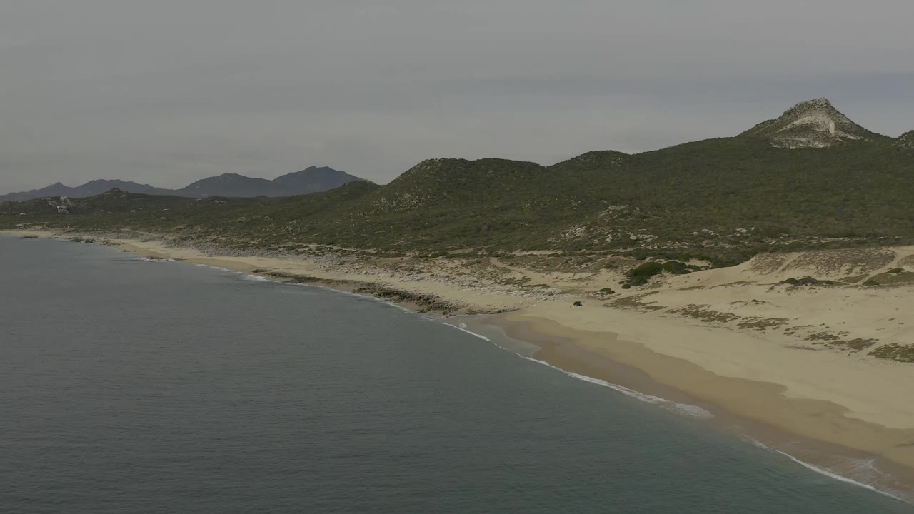 Baja California Sur beach from above, with calm water along the left edge, pale sand and dune ridges to the right, and no visible people.