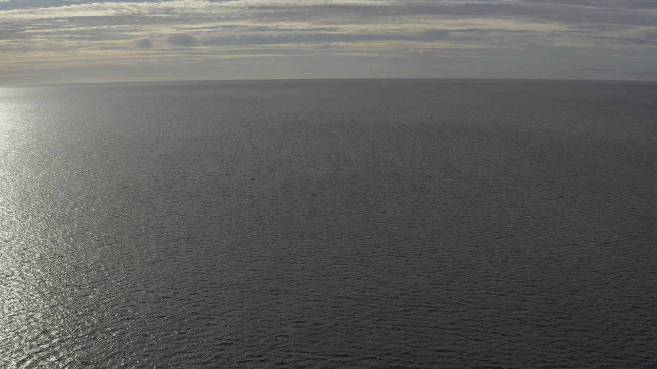 Baja California Sur ocean water fills the frame below a flat horizon, with a vertical strip of pale sun glare and muted gray clouds overhead, with no visible people.