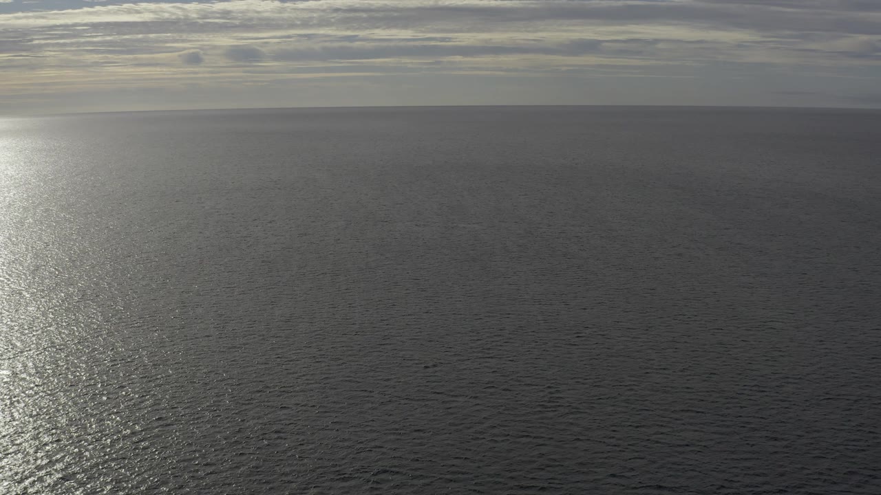Wide Baja California Sur seascape with the glare band pushed toward the left edge, dark open water across the center, cloud layers above, and no visible people.