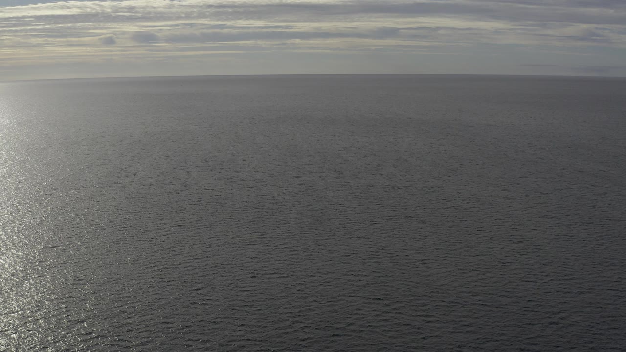 Wide view of the Baja California Sur ocean under layered clouds, with a bright vertical reflection on rippled water and no visible people.