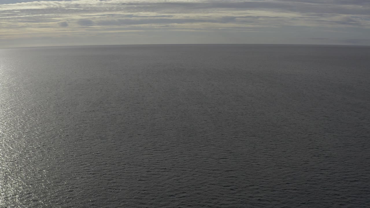 A wide Baja California Sur sea view shows gray-blue water below a banded cloudy sky, with soft sun shimmer on the surface and no visible people.