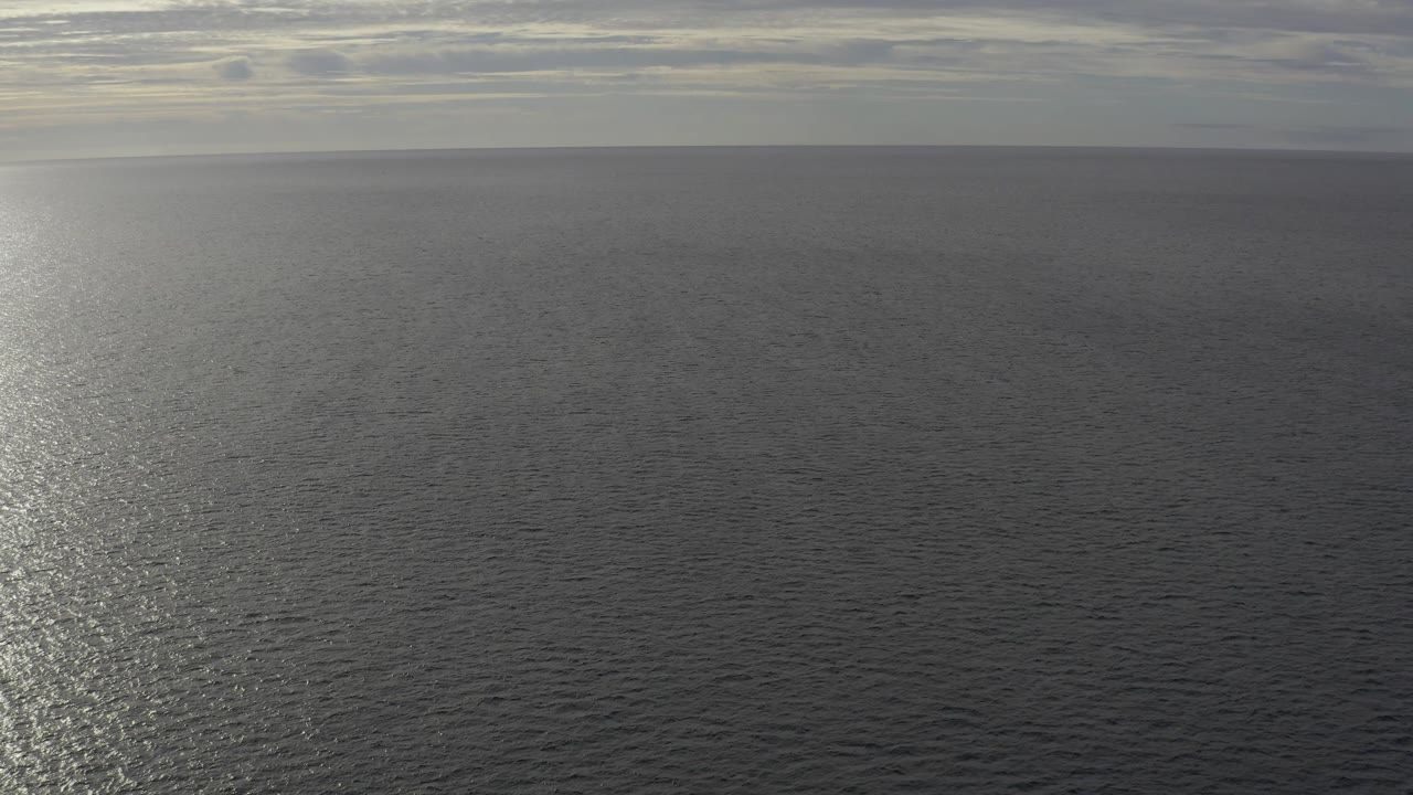 A wide view of Baja California Sur Mexico water shows the sunlight path nearer the center, with gray cloud layers above the horizon and no visible people.