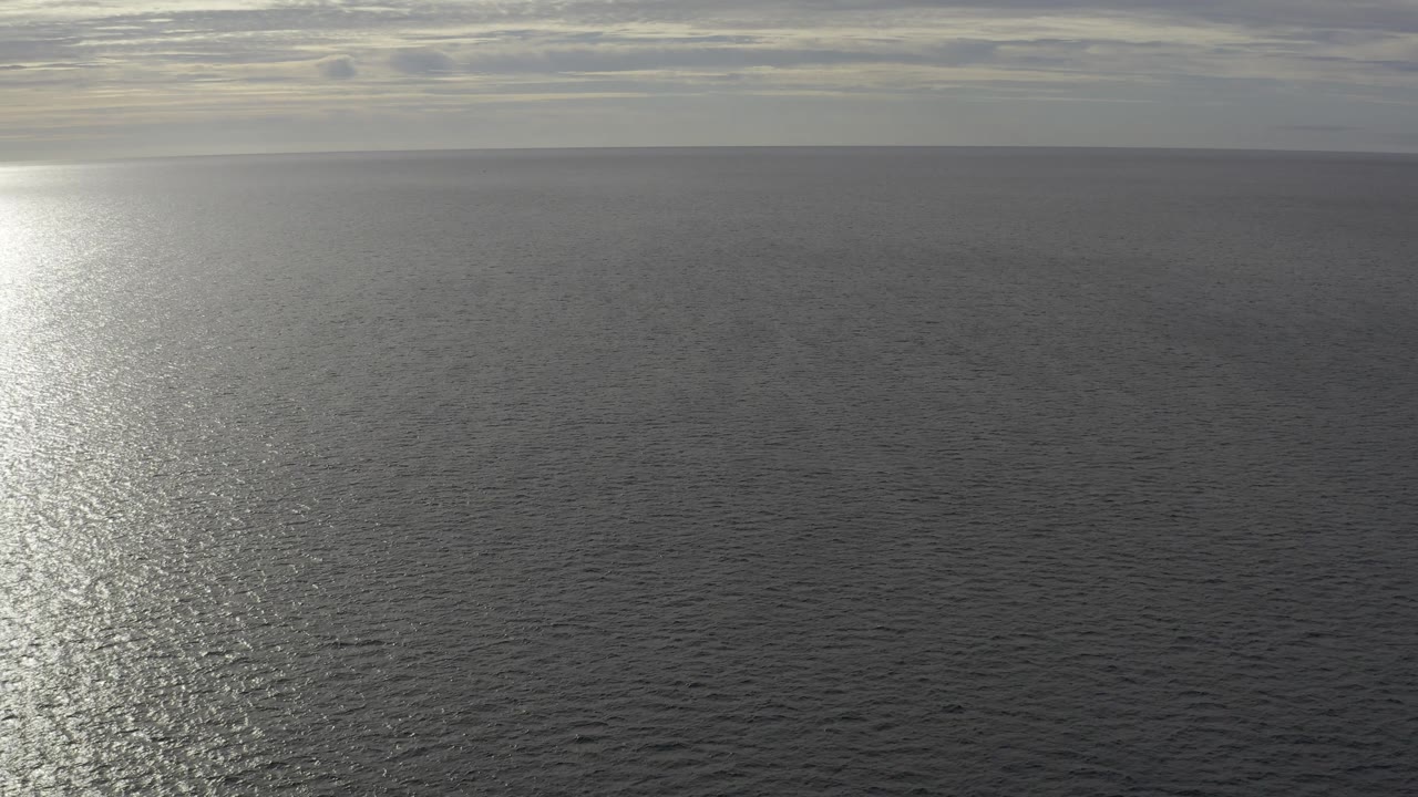 The Baja California Sur Mexico ocean fills most of the frame as a brighter vertical reflection spreads over dark ripples, with muted clouds on the horizon and no visible people.