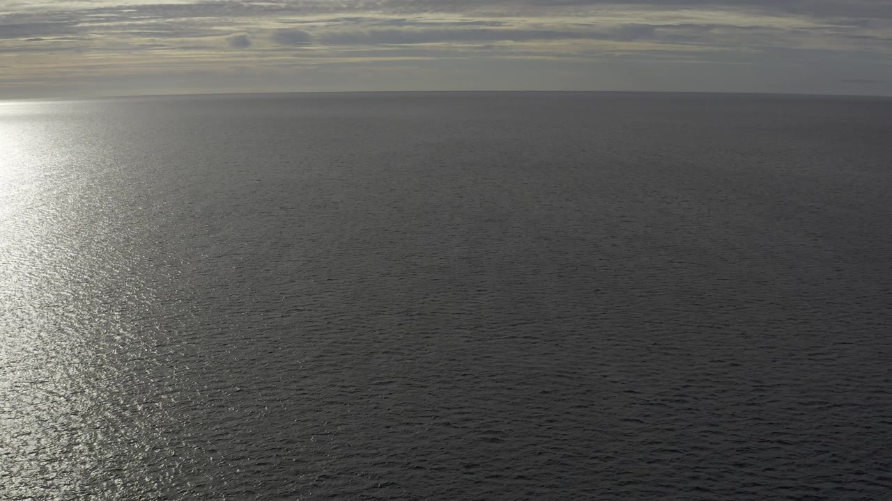 Aerial view of Baja California Sur open water with the sun reflection near the center, a dark sea surface, thin warm cloud breaks, and no visible people.