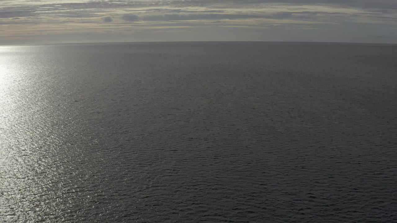 Wide East Cape ocean view with the horizon high in frame, small ripples across dark water, a pale vertical reflection closer to center-left, and no visible people.