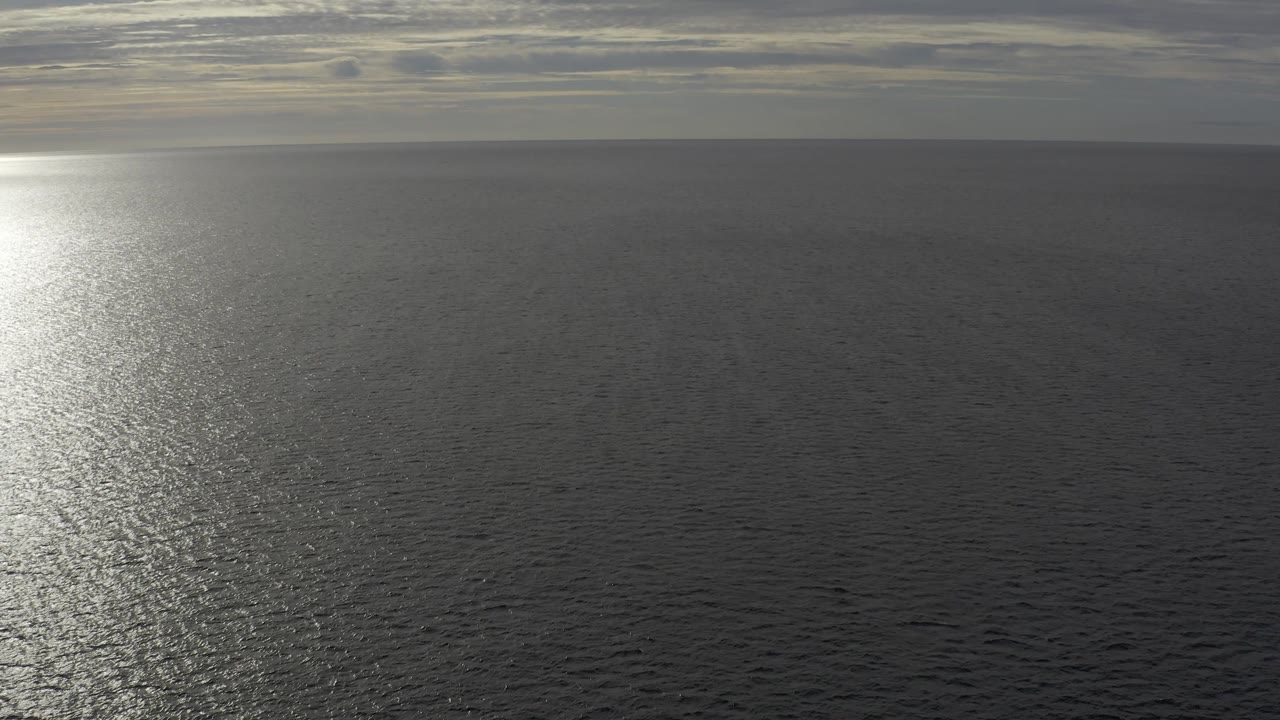 Baja California Sur seascape showing dark rippled water, a soft gray cloud ceiling, the horizon near the upper third, a bright reflection near center, and no visible people.