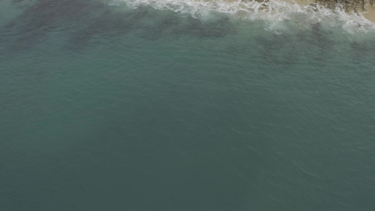 Overhead coastline with white wash breaking into blue-green water.
