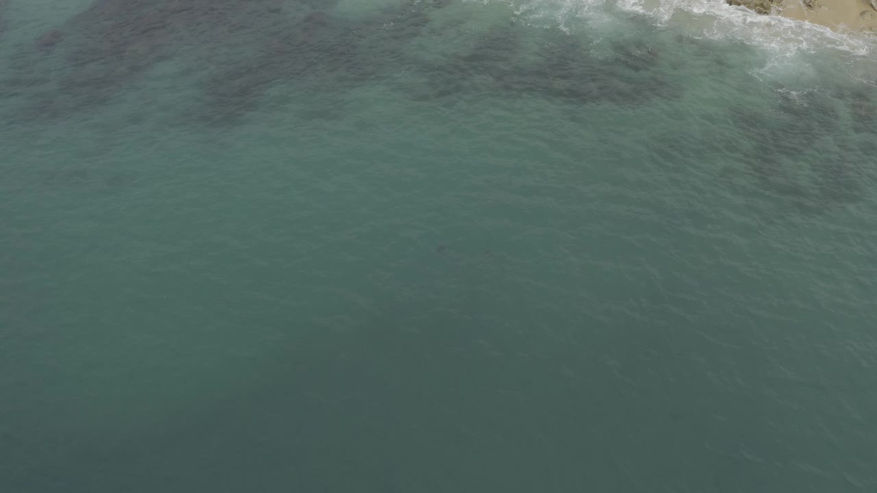 Aerial Baja California Sur, Mexico view with darker wind-textured patches in the green-blue water and white foam tracing the coast at the top, no visible people.