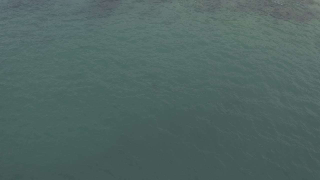 A flat green-blue ocean surface in Baja California Sur, Mexico fills the frame, with slightly darker ripples and no visible people.