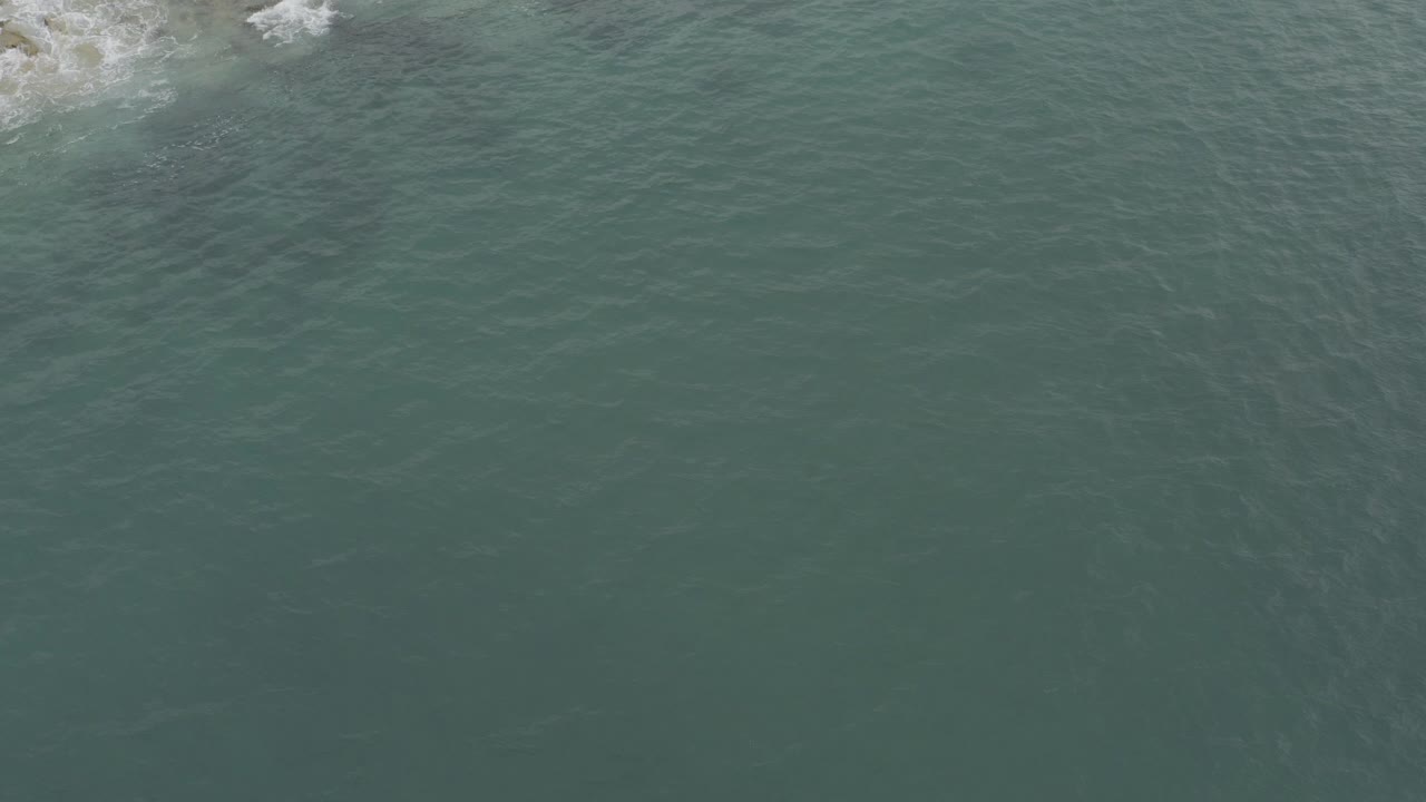 Aerial view of green-blue water beside a rocky wave line.