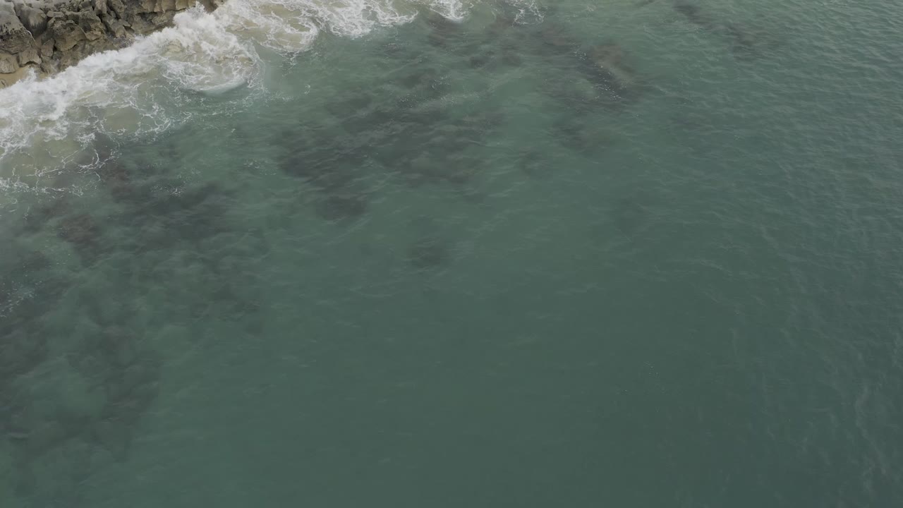 Aerial water with surf breaking along rocky shore