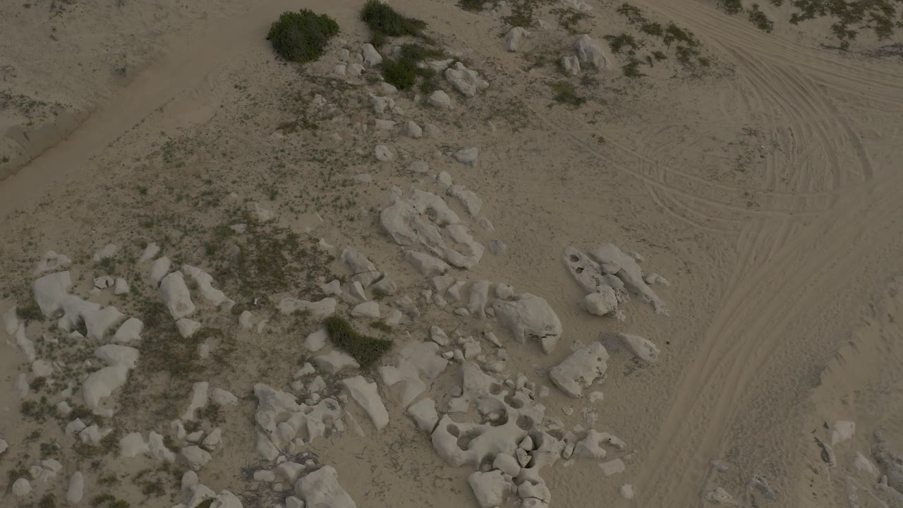 Top-down frame of Baja California Sur terrain with rounded rocks, sparse vegetation, a pale sand path, and no visible people.