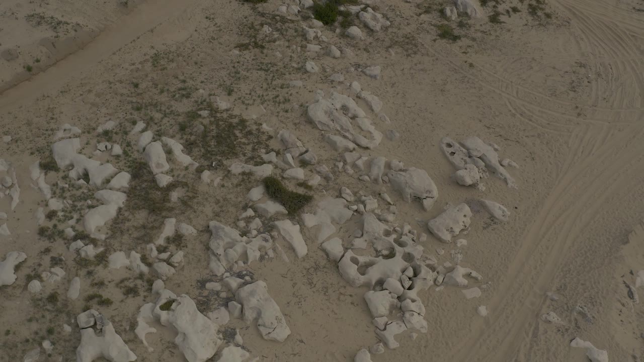 Third overhead frame of Baja California Sur terrain, with the boulder clusters shifted lower in frame and a track-marked sandy area running along the right side, with no visible people.