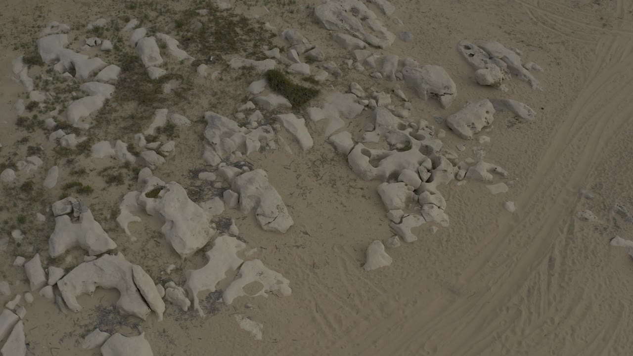 Aerial frame from Baja California Sur Mexico showing rounded pale rocks, low scrub vegetation, marked sandy ground, and no visible people.