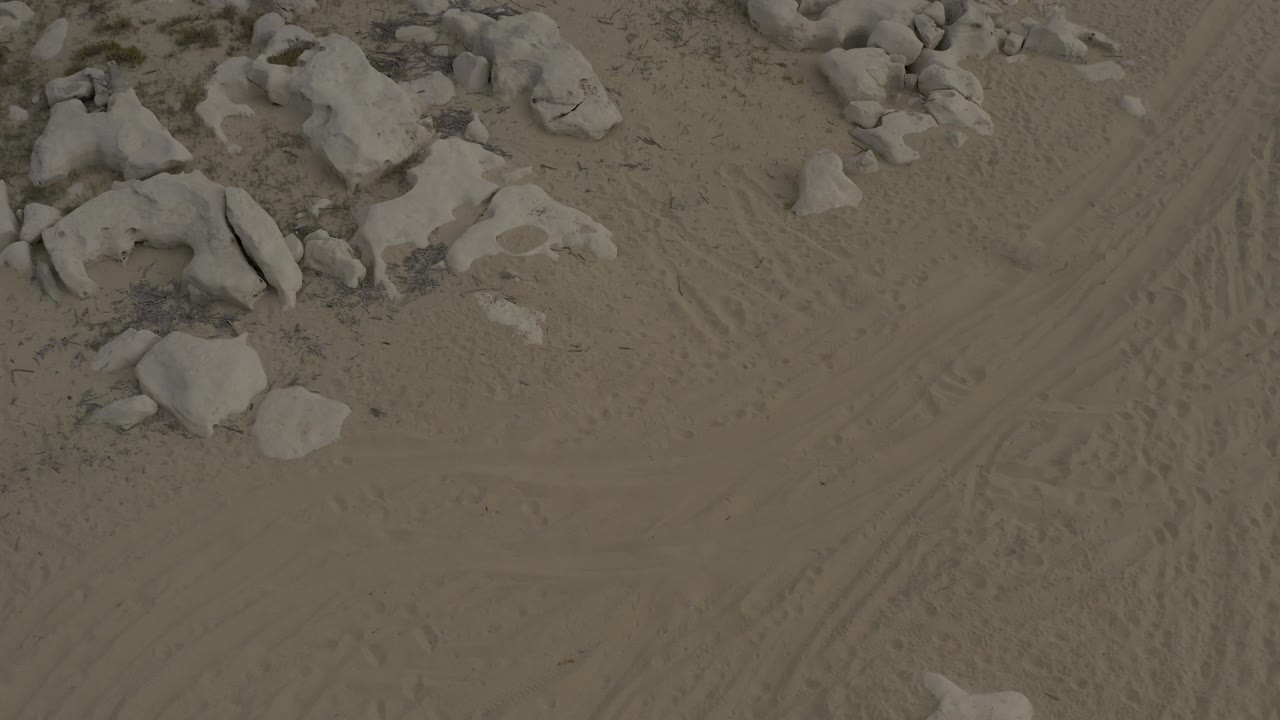 The third frame shows Baja California Sur desert sand with a cluster of pale rocks near the upper left and faint tire marks crossing the open center, no visible people.