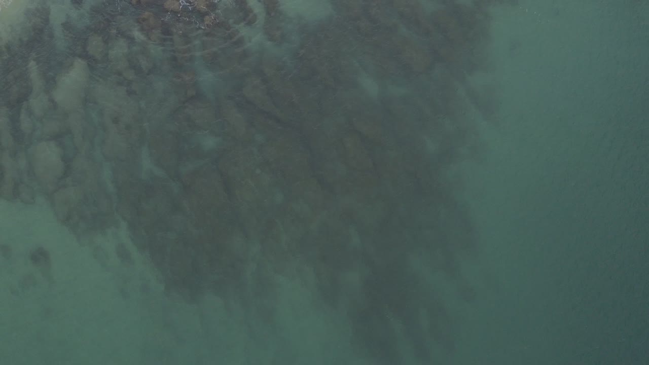 Bird's-eye frame over blue-green water and dark reef texture in Baja California Sur, Mexico, with no visible people.