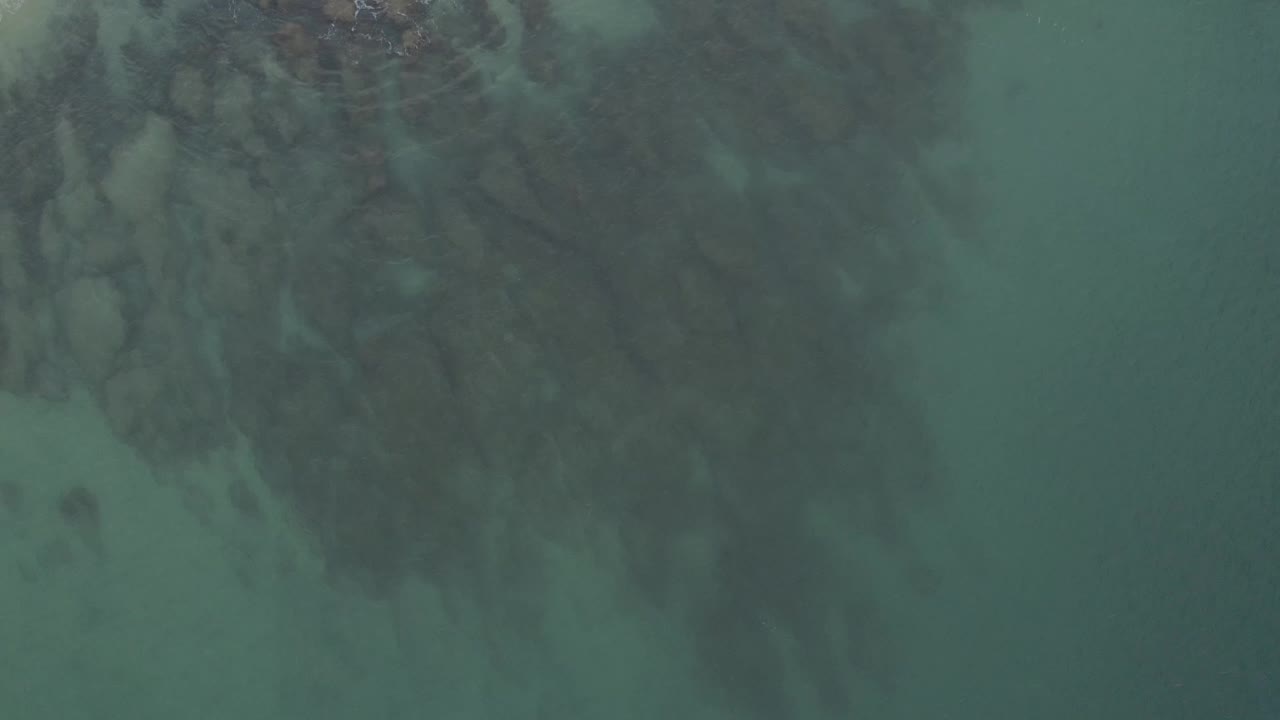 Aerial view of rippled water with a dark reef mass across the upper frame.