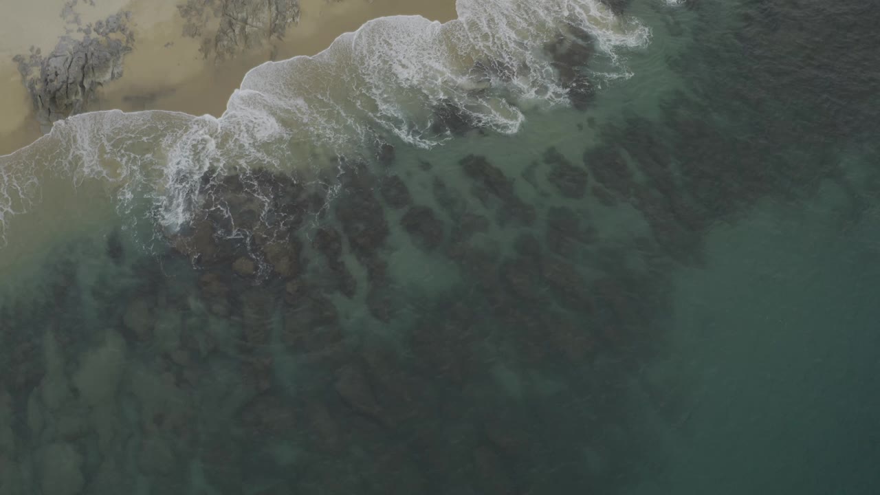 Aerial shoreline with foamy waves over rocks and clear water